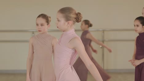 a group of young ballet students in black dancewear practicing positions in a spacious ballet studio with wooden flooring and wall-mounted barres. focused expressions and synchronized movements.