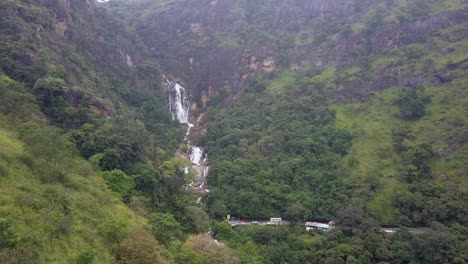 mountain forest aerial: highway traffic crosses bridge below waterfall