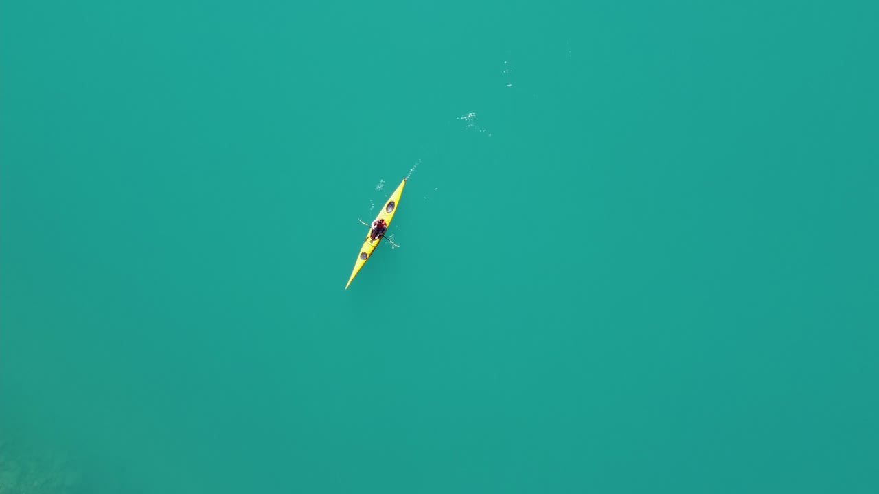 mujer navegando en kayak a través de agua limpia y vibrante del glaciar verde en kayak amarillo - vista aérea estática de ojo de pájaro con kayak pasando a través del marco - lago lovatnet en loen nordfjord noruega