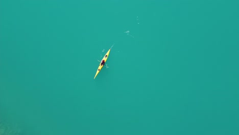 woman kayaking through clean vibrant green glacier water in yellow kayak - static birdseye aerial view with kayak passing through frame - lovatnet lake in loen nordfjord norway