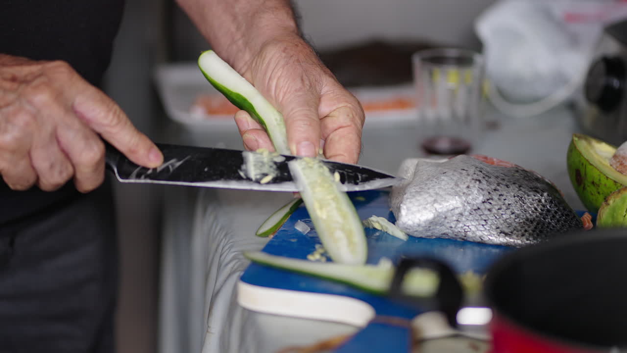 Slicing cucumber and fresh raw fish by hand with knife for salmon sashimi preparation. Close-up