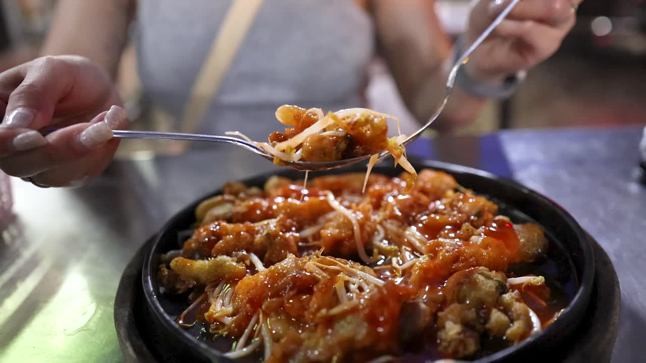 Person lifts sizzling fried oyster mussel dish with fork at vibrant Bangkok street food stall