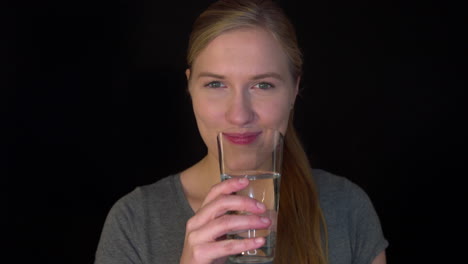 young woman is drinking clean fresh water from glass holding in her hand