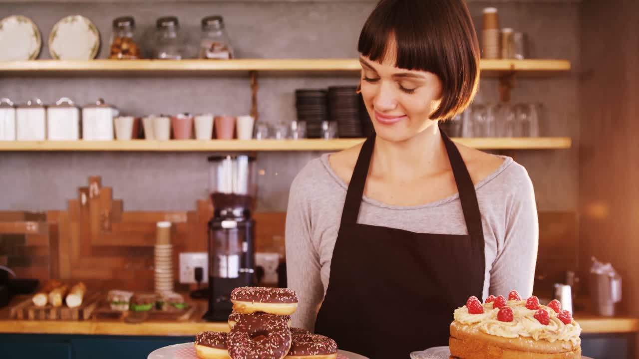 Portrett av servitrise som holder smultringer og kake på kafé