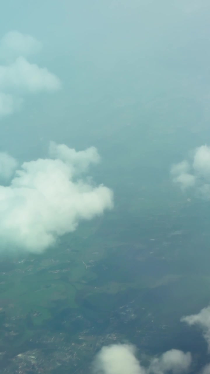 Vertical aerial view of soft white clouds floating above the landscape, creating a calm atmospheric scene with hazy blue tones and high-altitude perspective.