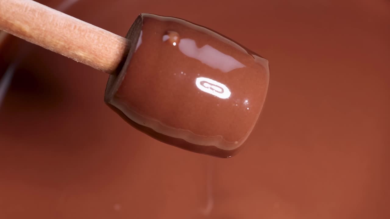 Close-up of a wooden spoon gently dipping into and lifting smooth, glossy chocolate.