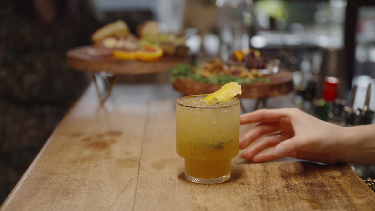 A mixologist hands as they serve a lemon cocktail in a gold rimmed glass onto the bar - in 60 fps.