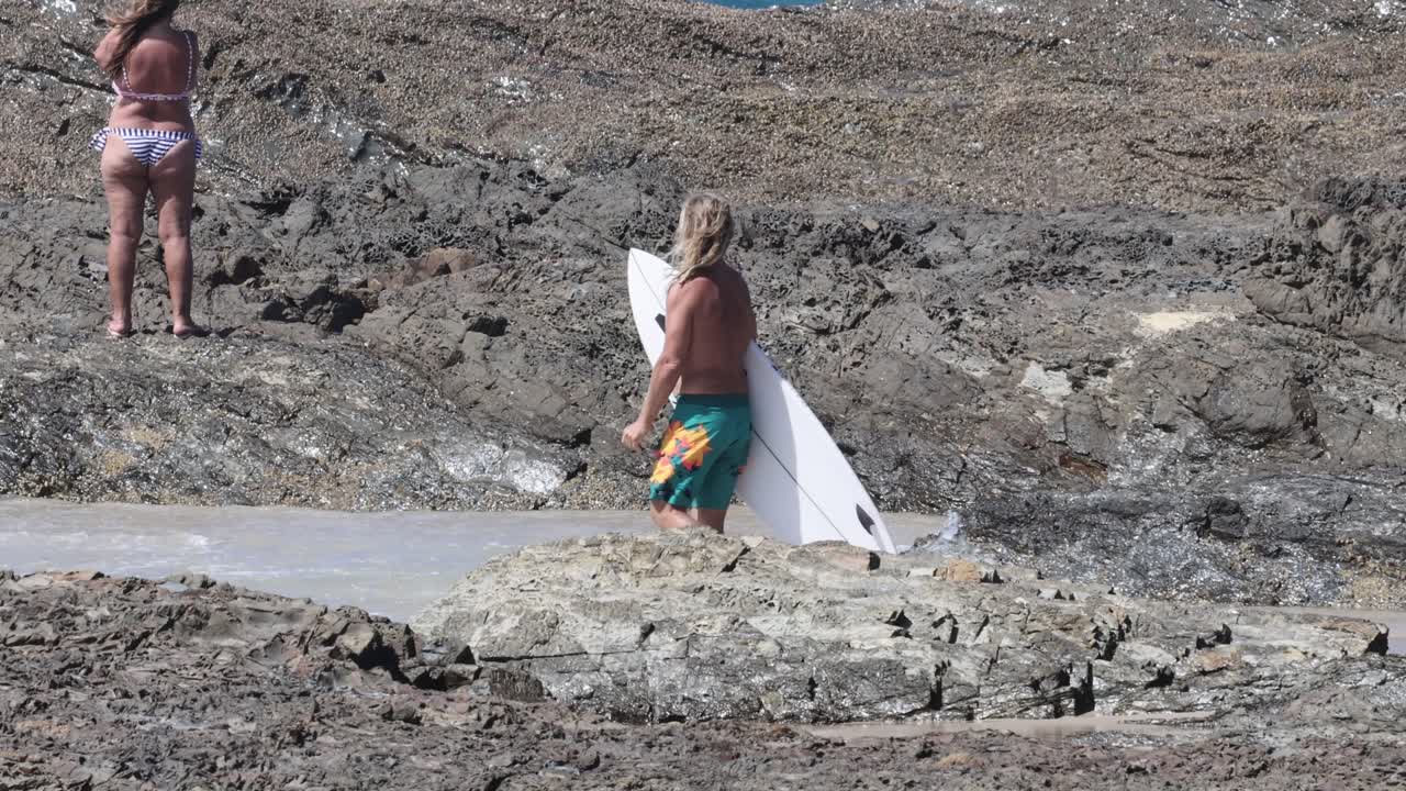 바위 가득 한 해변 을 따라 보드 를 들고 는 서퍼 들