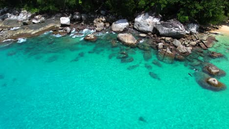 Video-De-Drone-De-2-Personas-Haciendo-Snorkel-Cerca-De-Enormes-Piedras-De-Granito,-Playa-De-Arena-Blanca,-Agua-Turquesa-Transparente-Del-Océano-Índico,-Mahe,-Seychelles-30fps