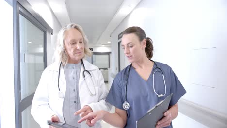 Caucasian-female-doctors-in-discussion-using-tablet-in-hospital-corridor,-slow-motion