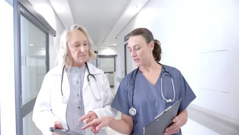 caucasian female doctors in discussion using tablet in hospital corridor, slow motion