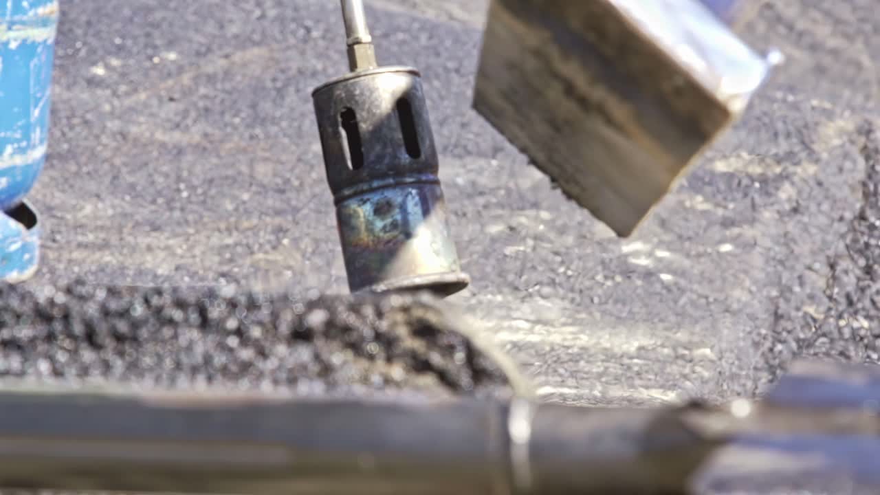 Gas torch and heavy roller compact hot asphalt during roadwork at construction site