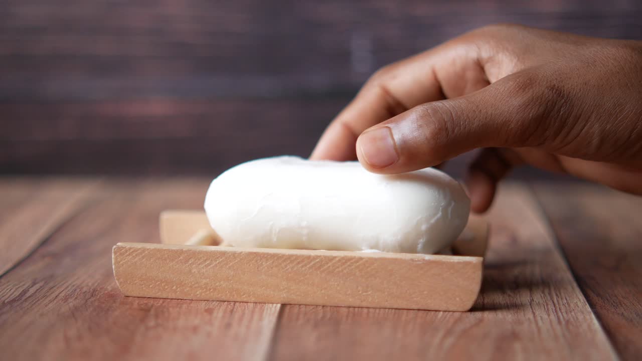 Person holding white bar of soap on a wooden tray