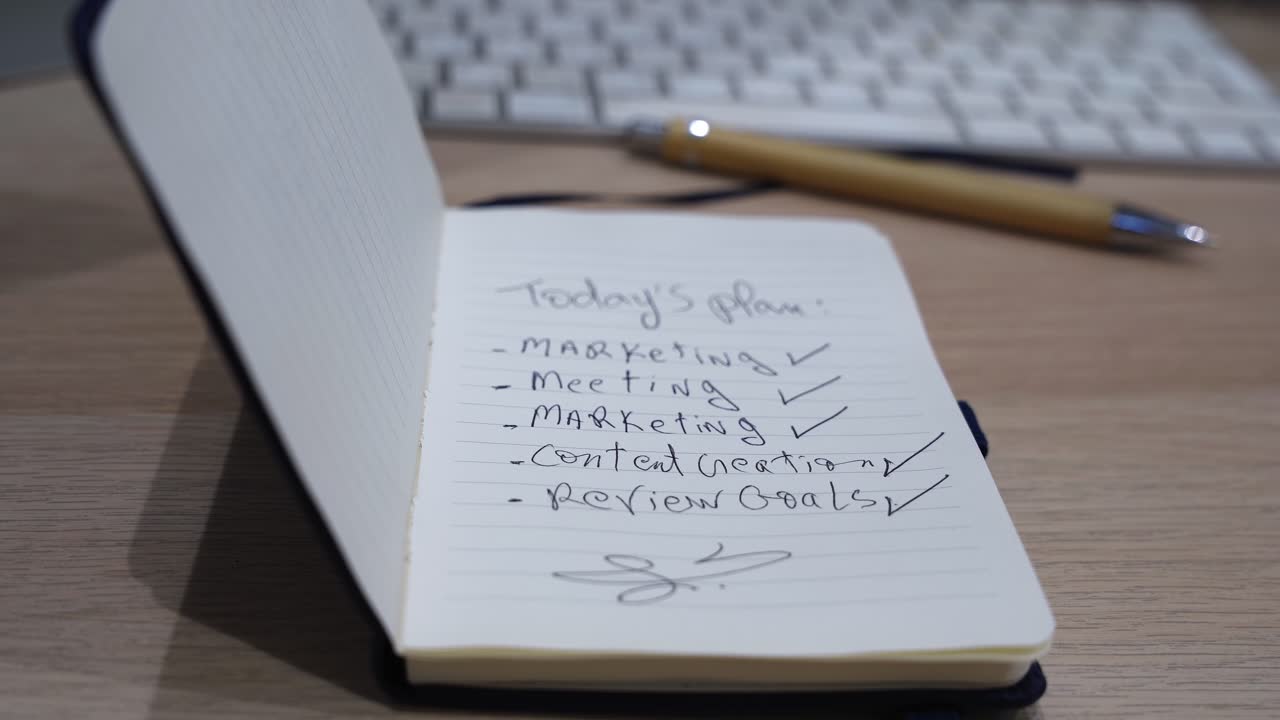 Detailed close-up of a handwritten daily plan in an open notebook on a wooden desk, with keyboard and pen in soft focus, showing workspace organization, productivity, and office planning