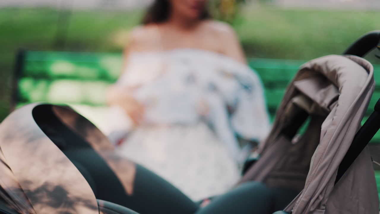 Close up of a stroller with a mother breastfeeding her baby while sitting on a park bench in the background