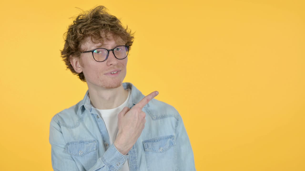 espacio de copia, joven pelirrojo señalando con el dedo, fondo amarillo