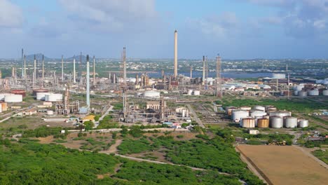 midday vibrant green tropical landscape disrupted by oil refinery flare stacks