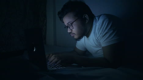 hombre indio trabajando horas extras usando la computadora portátil en la cama