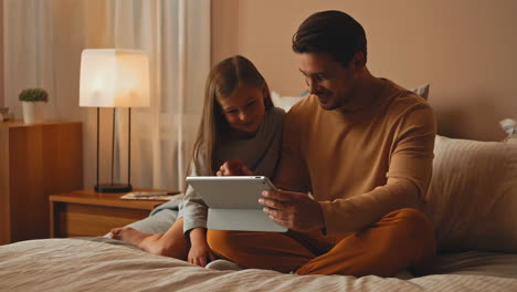 father and daughter using tablet in bedroom