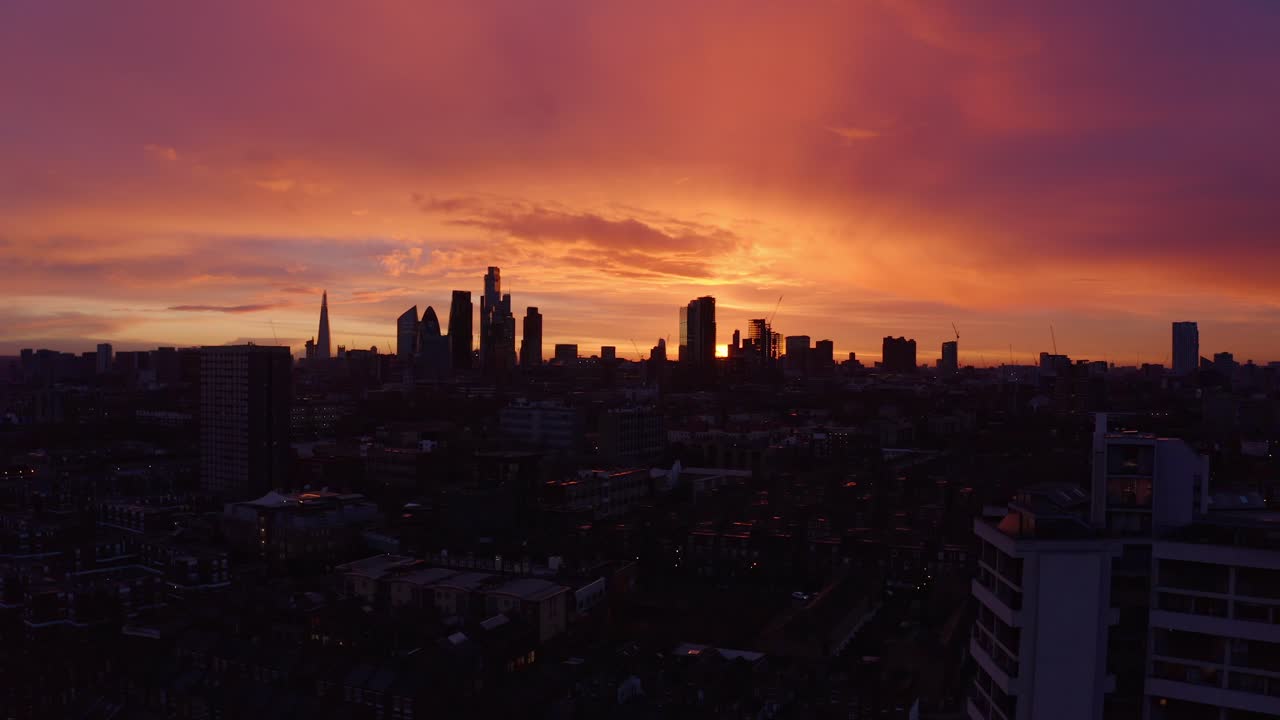 Toma aérea ascendente de dron desde edificios residenciales hacia los rascacielos del centro de Londres al atardecer.