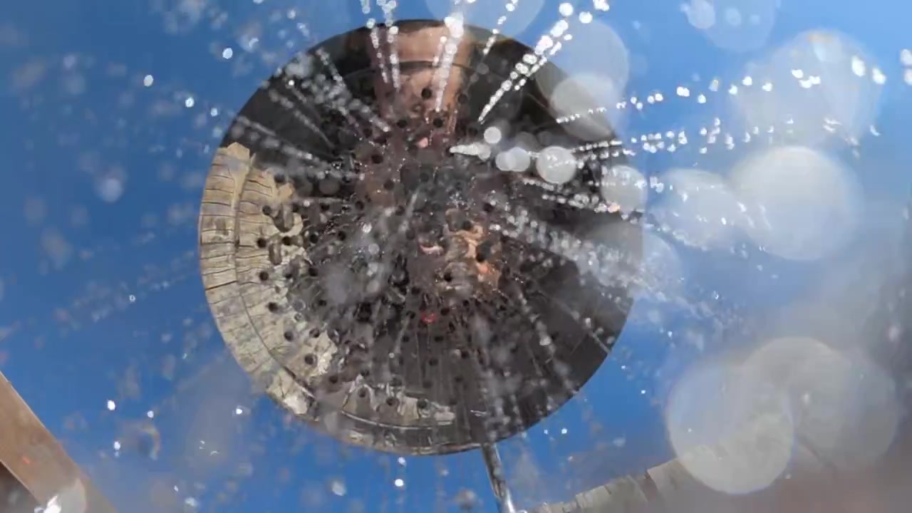 Shower head spraying refreshing water against a clear blue sky, creating a feeling of cleanliness and summer relaxation