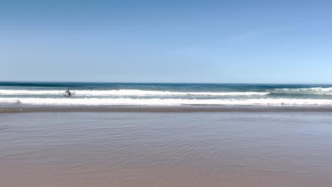 Surfer-going-into-the-sea-at-Caparica-Beach-during-a-sunny-day