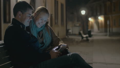 young couple using pad on the street bench