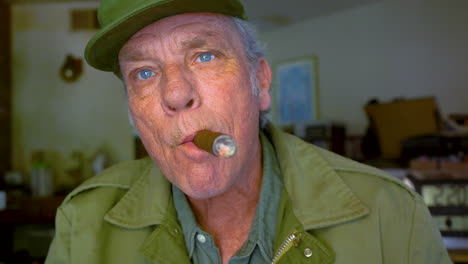 closeup of handsome mature male in his 60s smoking cigar and blowing smoke directly at the camera