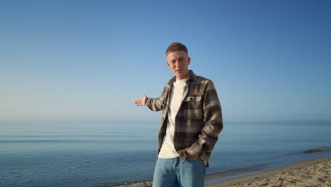 smiling man posing sunny seacoast. guy pointing hand on beautiful seascape.