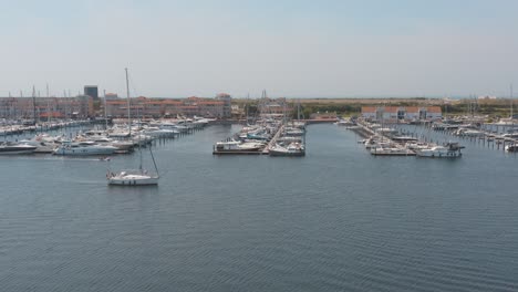 Cinematic-drone---aerial-panorama-shot-of-a-marina-with-sailing-boats-one-boat-sailing-in-the-foreground-on-a-sunny-day-at-Zeeland-at-the-north-sea,-Netherlands,-25p