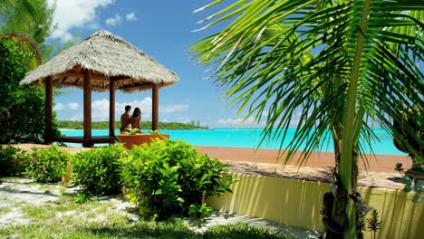 una pareja sentada en una cabaña de tiki con techo de paja en la playa