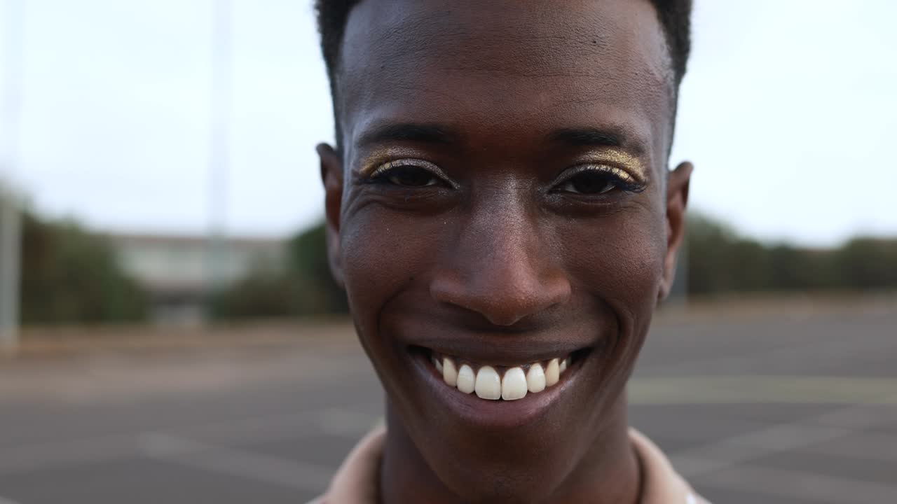 Happy gay african man with make-up smiling on camera outdoor