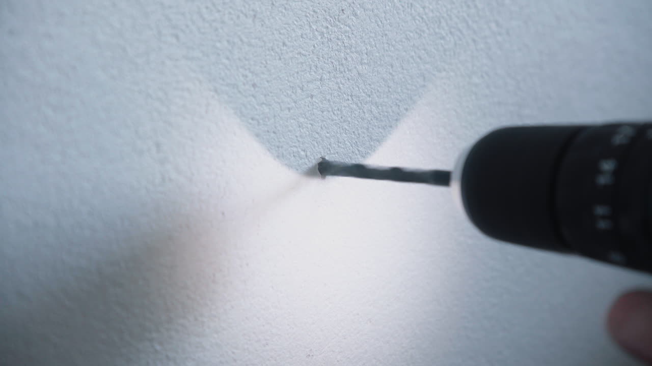 un joven manitas que usa un taladro eléctrico inalámbrico para perforar un agujero en una pared de cemento blanco, pero la pared es demasiado sólida y el taladro no entra en el detalle de la casa acerca el zoom en 4k