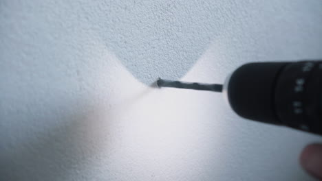 흰색 시멘트 콘크리트 벽에 구멍을 뚫기 위해 무선 전동 드릴을 사용하는 젊은 남성 잡역부