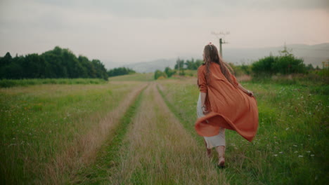 woman walking on a field road against a background of a forest and mountains