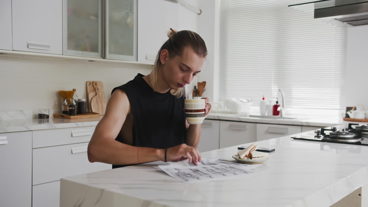 Young Male Stylist Checking Fashion Sketches during Breakfast