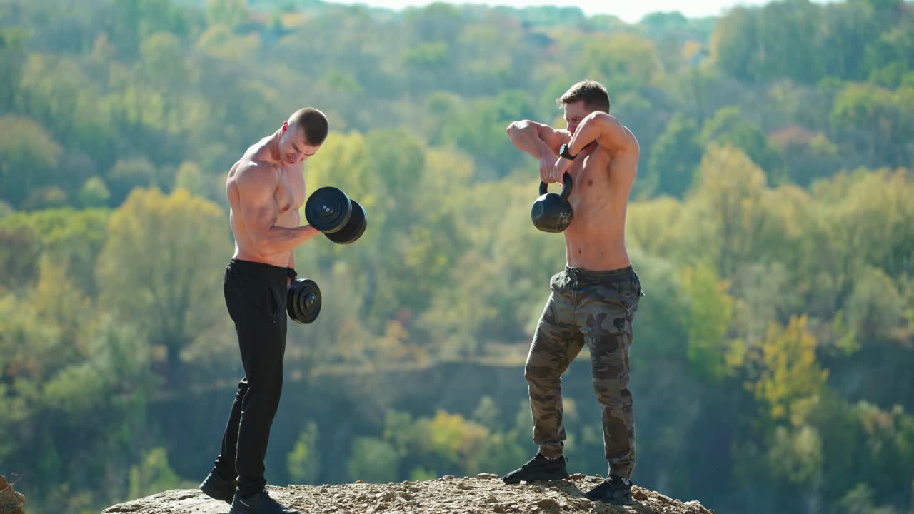 Shirtless sportsmen lifting weights outdoors. Muscular athletes training with dumbbells and kettlebell on nature background. Healthy lifestyle.