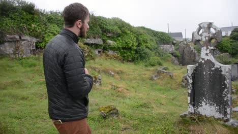 man in cemetery mourns in the rain over old blank tombstone