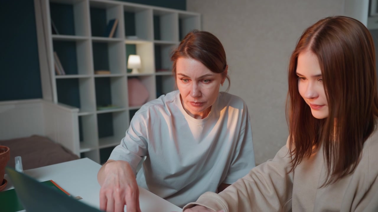 Kveldsveileder med laptop veileder student gjennom eksamensforberedelser, konsentrert tasting og peking på skjermen, skrivebordslampeglød, rolig studiestemning, planlegging og gjennomgang av oppgaver, bestemt