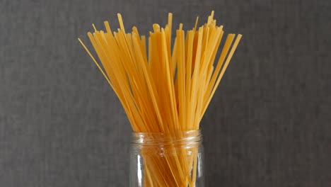 stick spaghetti pasta uncooked in a jar against grey background, closeup