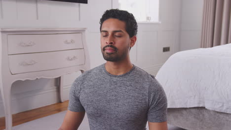 Dolly-shot-of-man-sitting-on-yoga-mat-in-bedroom-at-home-joining-hands-together---shot-in-slow-motion