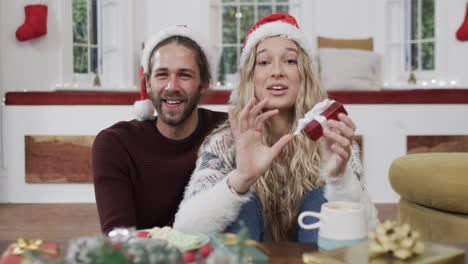 happy diverse couple wearing santa hats having christmas video call at home, in slow motion