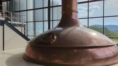 View-Of-Large-Copper-Brewing-Kettle-Indoor-At-Brewing-Factory-With-Clouds-Seen-Through-Windows-In-Background