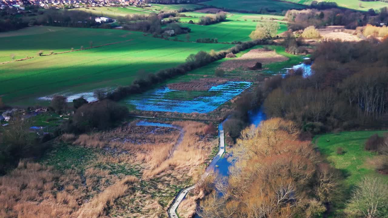 Letecký pohled z dronu na řeku vinoucí se mokřady a zemědělskou půdou v anglickém venkově. Přírodní krajina s poli, stromy a vodními kanály ve venkovské Velké Británii