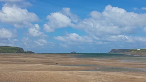 View-from-Daymer-Bay-towards-Steppers-Point-on-left-and-Trebetherick-Point-on-Right-at-low-tide,-golden-sand-in-foreground,-sunny-day