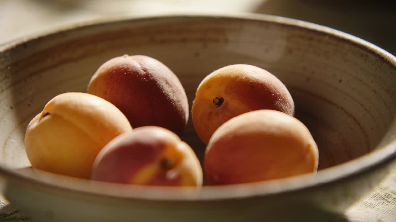 Vidéo verticale: Animée par une lumière douce, la caméra refocalise sur un bol posé sur une table, révélant des abricots