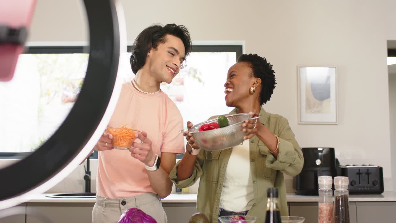 Diverse cooking cohosts holding bowls of carrots and peppers in kitchen starting cooking tutorial