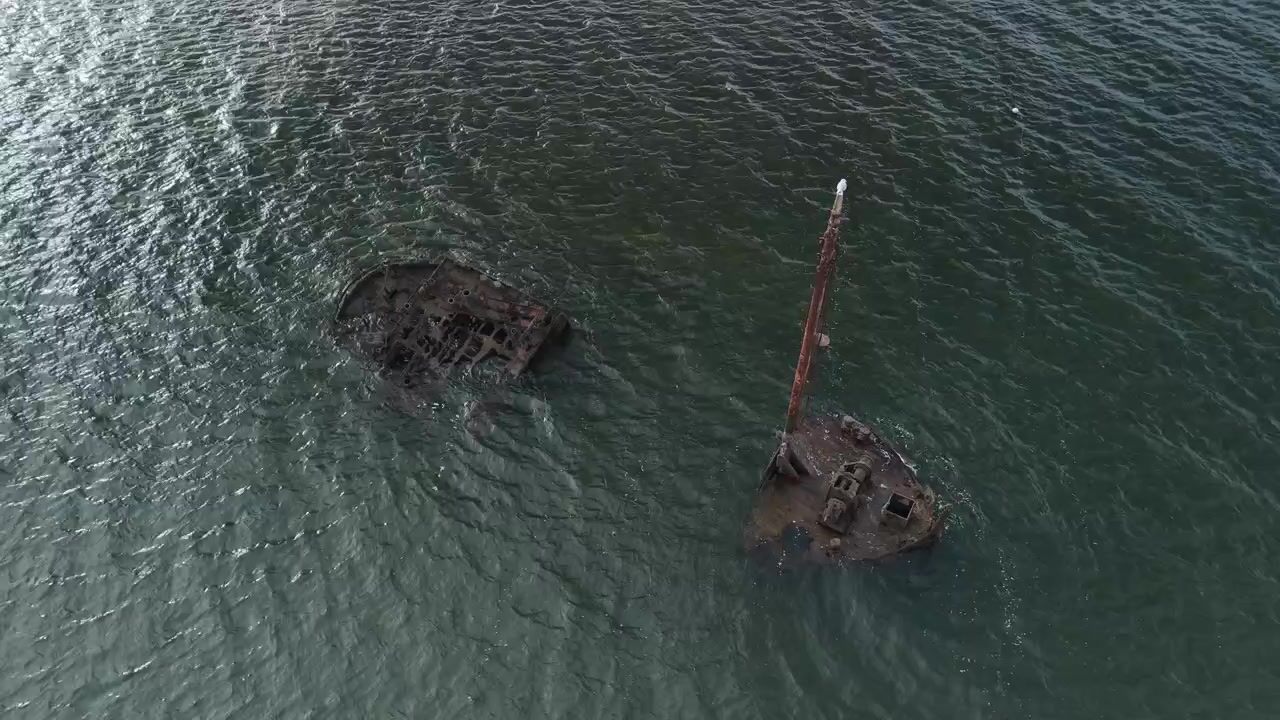 Static aerial of a rusting shipwreck sitting in deep green water, Scotland.