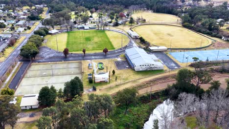 aerial footage captures a smooth drone flyover above sports fields, tennis courts, and surrounding suburban streets in coonabarabran, new south wales, under daylight