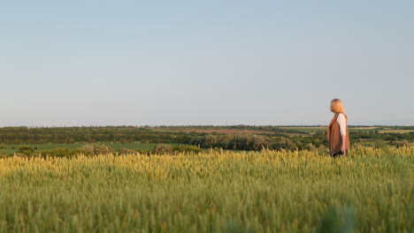 una mujer camina a través de un campo de trigo contra el telón de fondo de un pintoresco paisaje rural